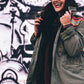 woman wearing olive green jacket in front of graffiti 
